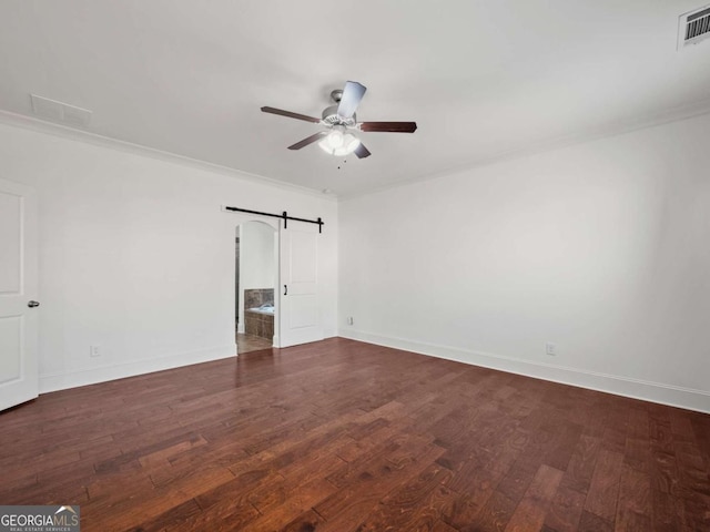 empty room featuring dark wood-type flooring, ornamental molding, a barn door, and ceiling fan