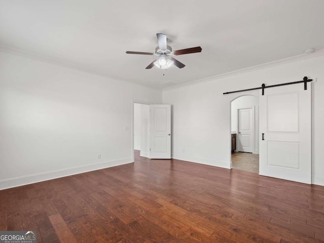 empty room featuring ornamental molding, a barn door, dark wood-type flooring, and ceiling fan