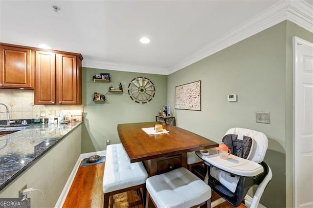 dining room featuring sink, wood-type flooring, and ornamental molding