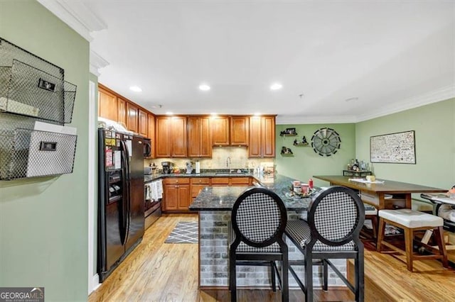 kitchen featuring light hardwood / wood-style floors, crown molding, black appliances, and kitchen peninsula