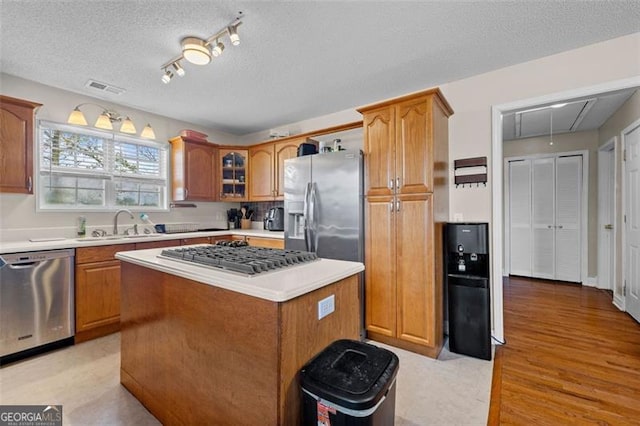 kitchen featuring sink, a center island, light hardwood / wood-style floors, stainless steel appliances, and a textured ceiling