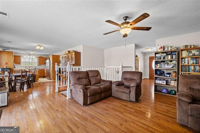 living room with ceiling fan, a textured ceiling, and light hardwood / wood-style floors