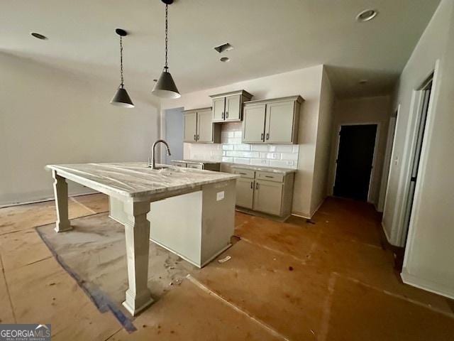 kitchen with gray cabinetry, hanging light fixtures, a kitchen island with sink, light stone countertops, and a kitchen bar