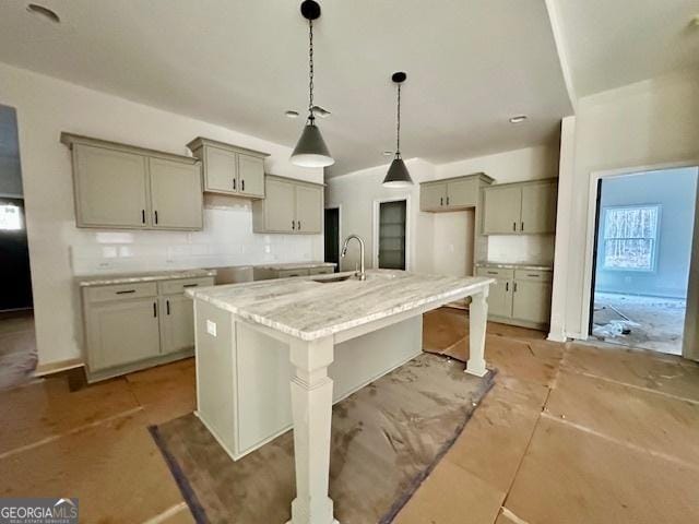 kitchen with light stone counters, sink, gray cabinets, and an island with sink