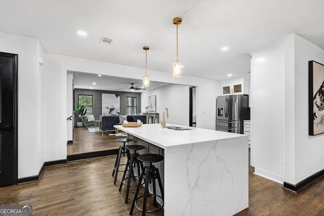 kitchen with decorative light fixtures, white cabinetry, sink, stainless steel fridge, and light stone countertops