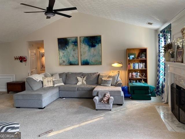 carpeted living room featuring a premium fireplace, vaulted ceiling, ceiling fan, and a textured ceiling