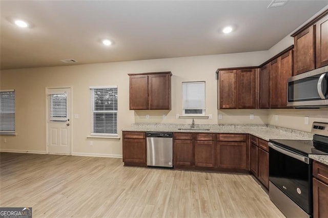 kitchen with sink, light stone counters, stainless steel appliances, dark brown cabinets, and light wood-type flooring