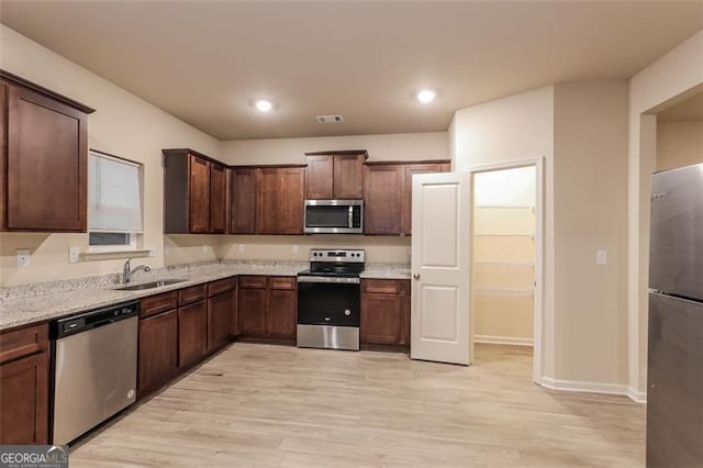 kitchen featuring light stone counters, sink, light wood-type flooring, and appliances with stainless steel finishes