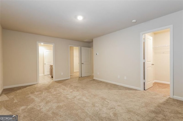 unfurnished bedroom with connected bathroom, a spacious closet, light colored carpet, and a closet