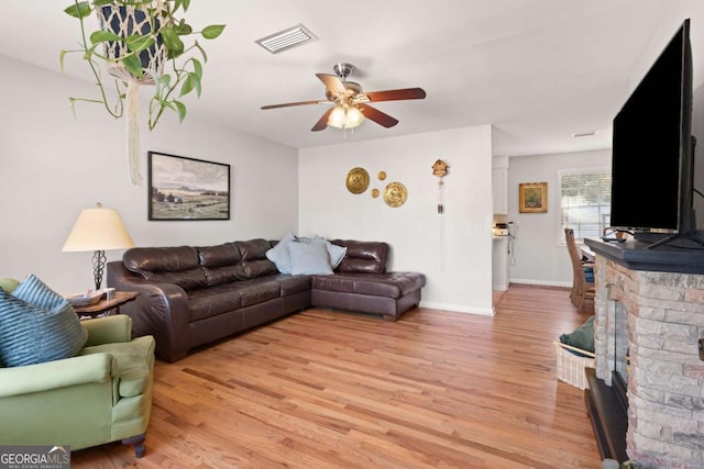 living room featuring a fireplace, light hardwood / wood-style floors, and ceiling fan