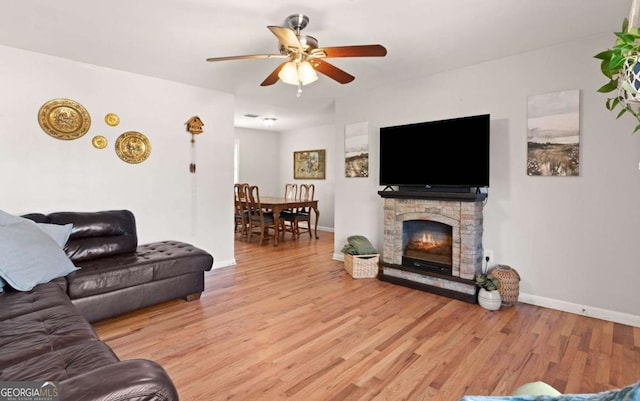 living room featuring ceiling fan, a fireplace, and light wood-type flooring