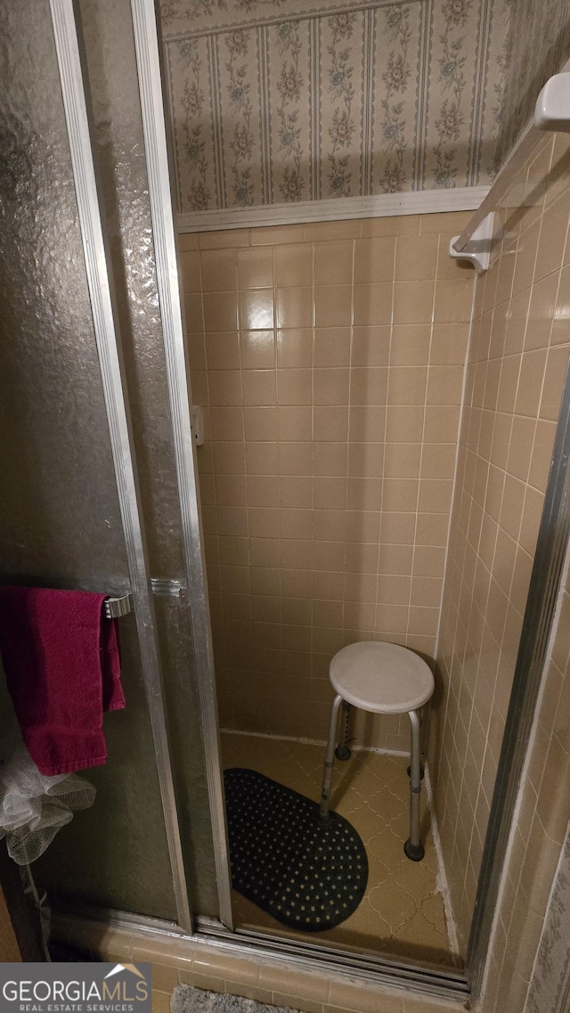 bathroom with a shower with shower door, tile patterned flooring, and tile walls