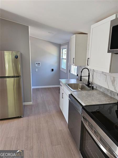 kitchen with appliances with stainless steel finishes, sink, white cabinets, decorative backsplash, and light hardwood / wood-style floors