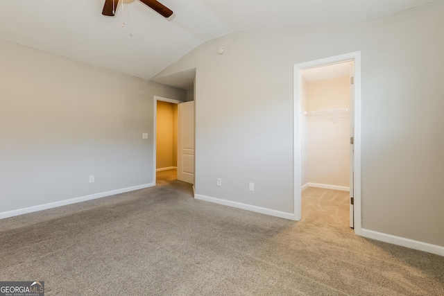 unfurnished bedroom with a walk in closet, vaulted ceiling, light carpet, a closet, and ceiling fan