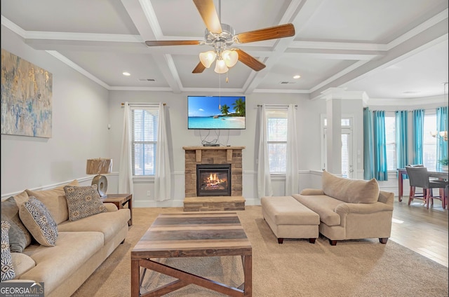 living room featuring coffered ceiling, a stone fireplace, ornamental molding, and beamed ceiling