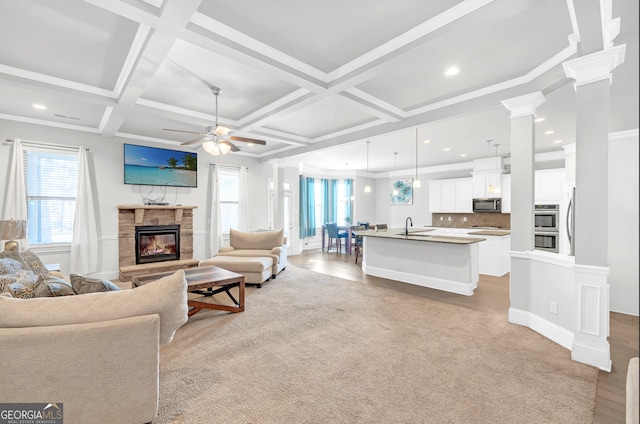 living room featuring a stone fireplace, beamed ceiling, sink, coffered ceiling, and ceiling fan