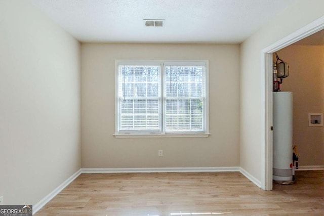 empty room featuring gas water heater, a textured ceiling, and light wood-type flooring