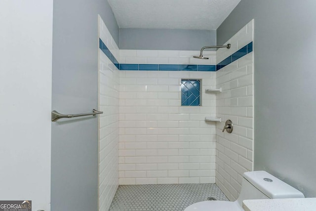 bathroom with toilet, a textured ceiling, and a tile shower