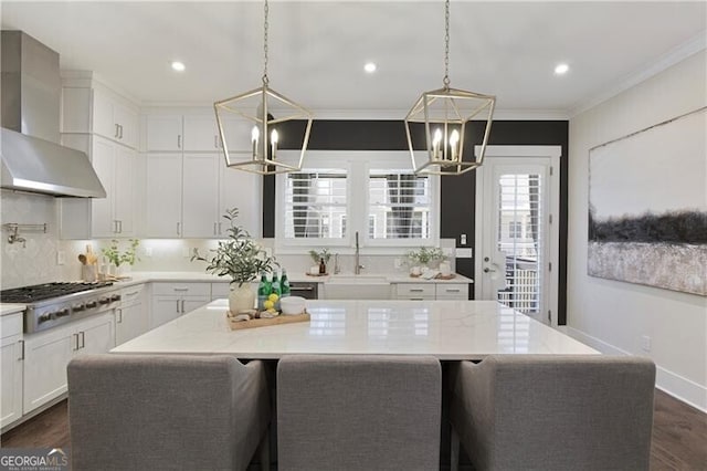 kitchen with wall chimney range hood, sink, hanging light fixtures, a center island, and stainless steel gas stovetop