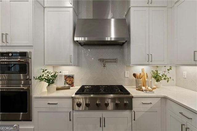 kitchen with white cabinetry, appliances with stainless steel finishes, decorative backsplash, and wall chimney range hood