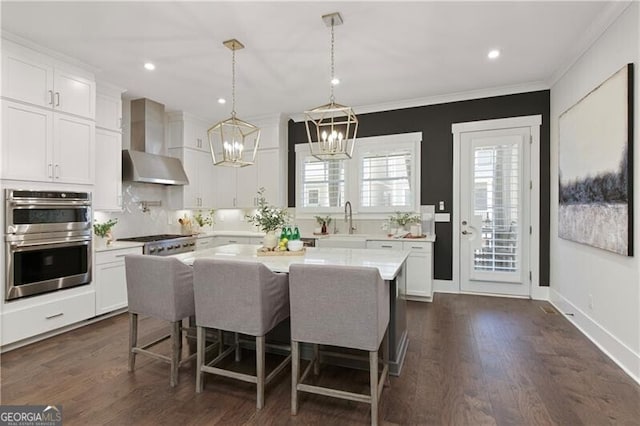 kitchen featuring wall chimney range hood, stainless steel appliances, white cabinets, and a kitchen island