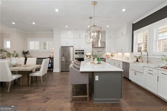 kitchen featuring white cabinetry, sink, a center island, stainless steel appliances, and wall chimney range hood