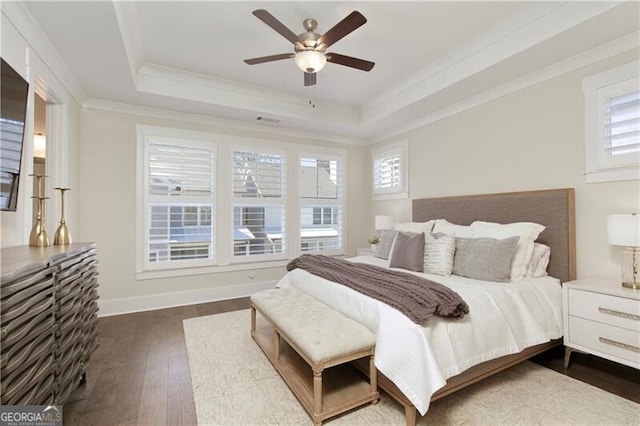 bedroom with crown molding, dark hardwood / wood-style floors, a tray ceiling, and ceiling fan