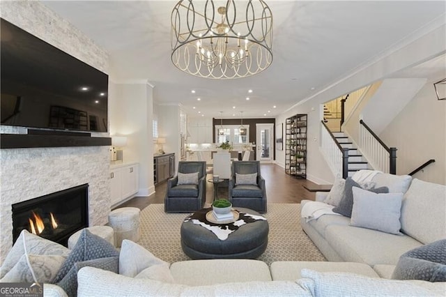 living room featuring crown molding, a stone fireplace, hardwood / wood-style floors, and a notable chandelier