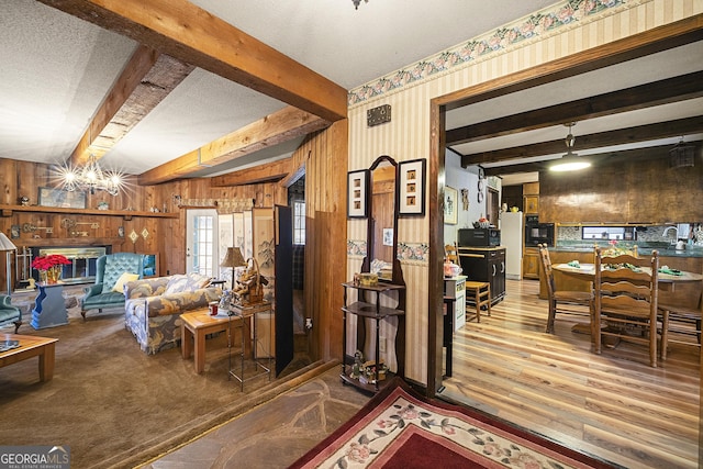 living room with beamed ceiling, wood-type flooring, wooden walls, and a textured ceiling