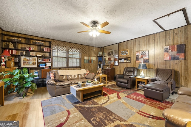 living room with ceiling fan, wood-type flooring, a textured ceiling, and wood walls