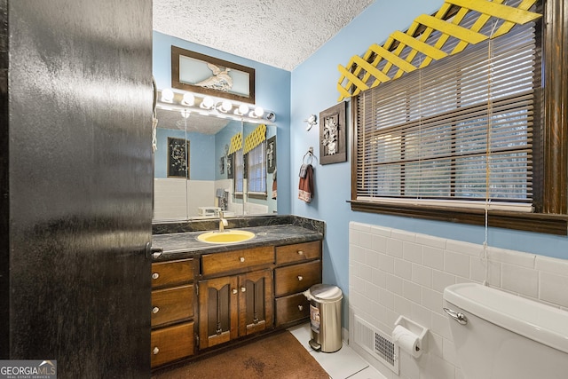 bathroom featuring tile walls, tile patterned flooring, vanity, toilet, and a textured ceiling