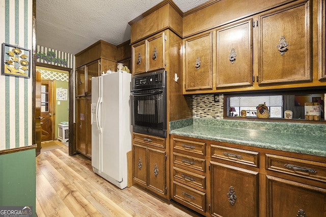 kitchen featuring black oven, tasteful backsplash, white refrigerator with ice dispenser, a textured ceiling, and light hardwood / wood-style flooring