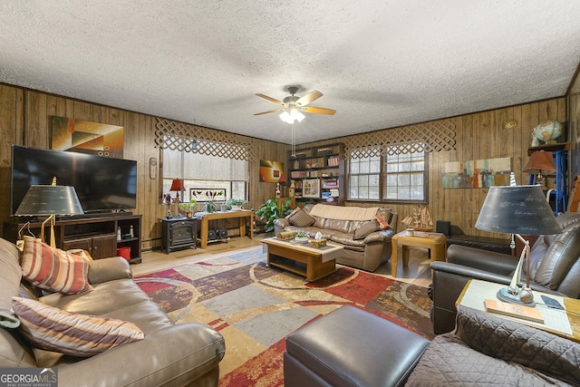 living room featuring ceiling fan, wooden walls, light hardwood / wood-style floors, a textured ceiling, and a wood stove