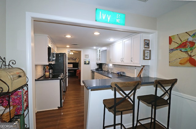 kitchen with sink, a breakfast bar area, white cabinetry, dark hardwood / wood-style floors, and kitchen peninsula