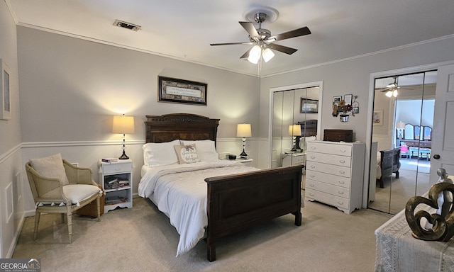 carpeted bedroom featuring crown molding, two closets, and ceiling fan