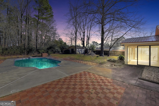 pool at dusk with a shed, a patio area, and a diving board