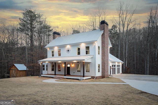 view of front of home with a storage shed, a chimney, metal roof, an outbuilding, and a porch