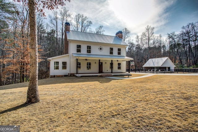 back of property with ceiling fan, metal roof, a chimney, and a lawn