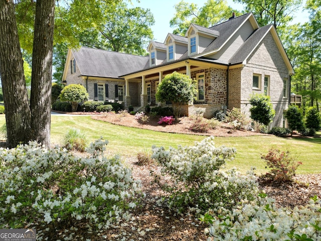 cape cod house with covered porch, brick siding, a front yard, and roof with shingles