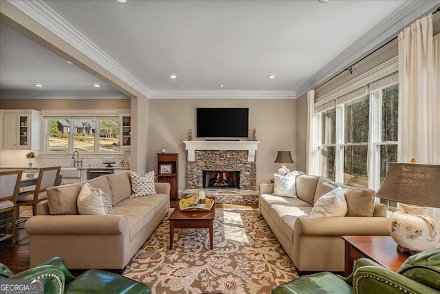 living room with ornamental molding, a stone fireplace, sink, and light hardwood / wood-style floors