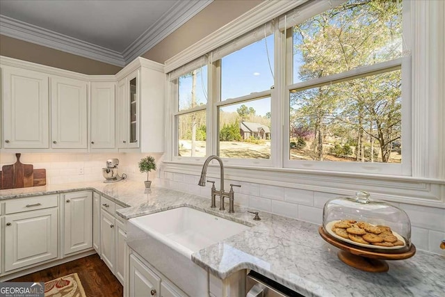 kitchen with sink, crown molding, light stone counters, white cabinets, and decorative backsplash