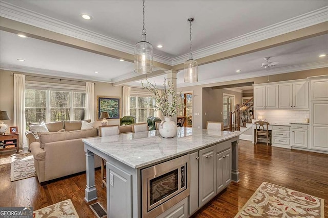 kitchen with stainless steel microwave, a kitchen island, pendant lighting, light stone countertops, and white cabinets