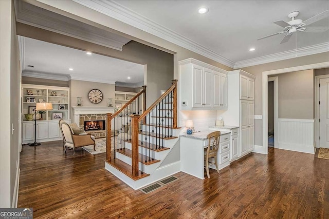 staircase featuring hardwood / wood-style flooring, a fireplace, ornamental molding, and ceiling fan