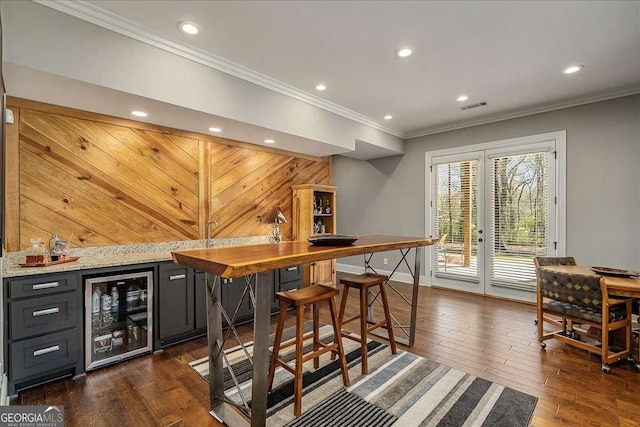 bar with beverage cooler, a dry bar, french doors, ornamental molding, and dark wood-type flooring
