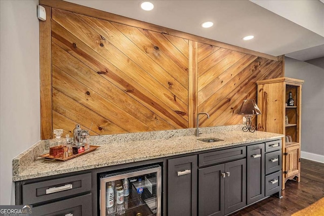 bar featuring sink, dark wood-type flooring, light stone countertops, and beverage cooler