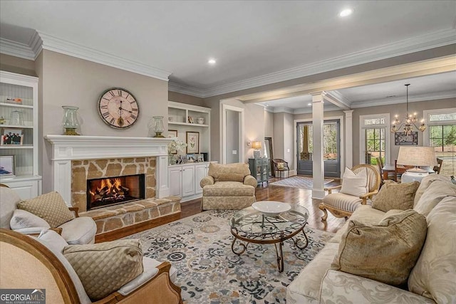 living room with an inviting chandelier, wood finished floors, ornamental molding, decorative columns, and built in shelves
