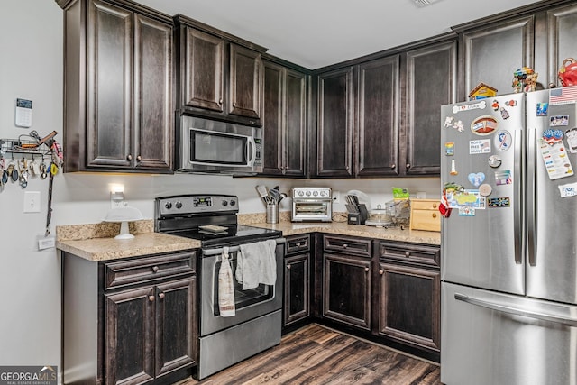 kitchen featuring stainless steel appliances, light stone countertops, dark brown cabinets, and dark hardwood / wood-style floors