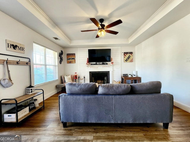 living room featuring crown molding, a large fireplace, dark hardwood / wood-style flooring, a raised ceiling, and ceiling fan