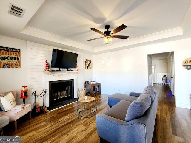 living room with a raised ceiling, crown molding, hardwood / wood-style floors, and a fireplace