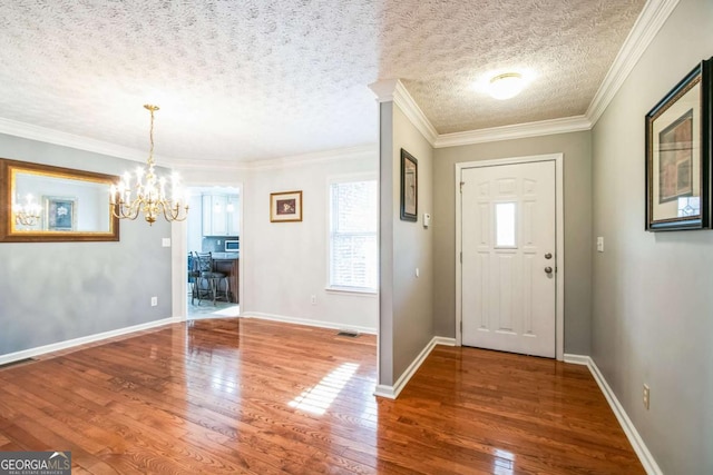 foyer with an inviting chandelier, ornamental molding, hardwood / wood-style floors, and a textured ceiling